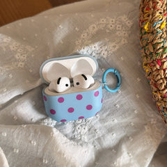 An open blue polka dot AirPods case displaying two white wireless earbuds inside, set against a white lace background.