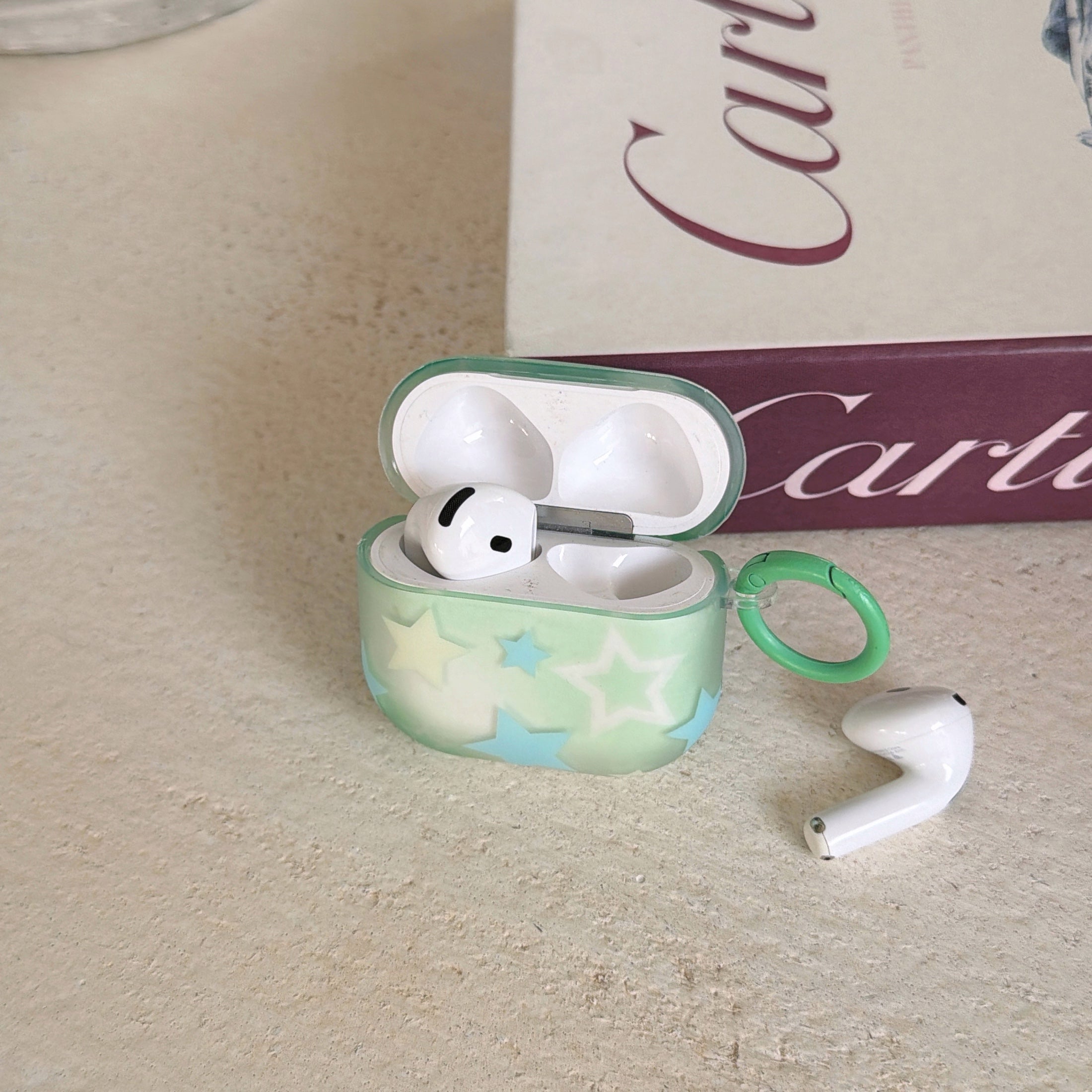 An open translucent mint green star AirPods case with one wireless earbud inside and one next to it.