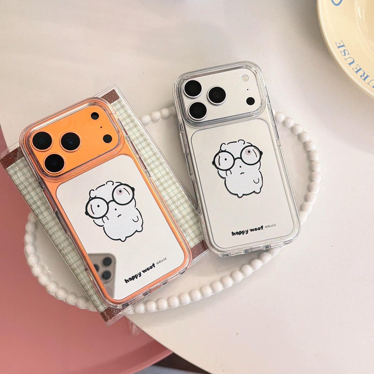 Two cartoon mirror iphone cases with orange and silver camera blocks side-by-side on a tray.