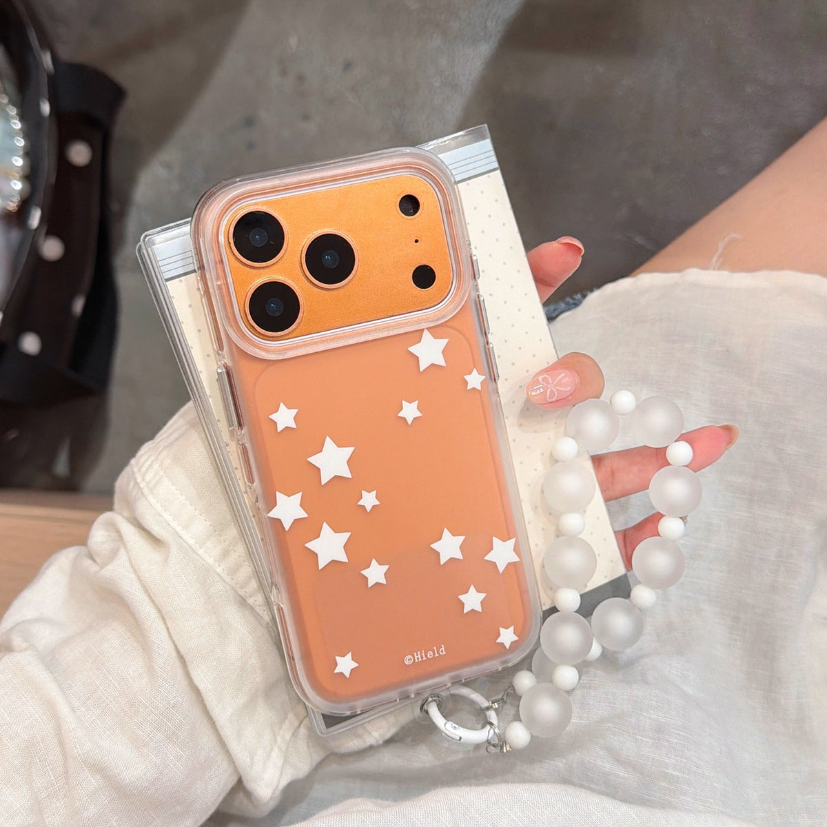 A close-up of a hand holding an orange phone case with white stars and an orange metallic camera lens shield.