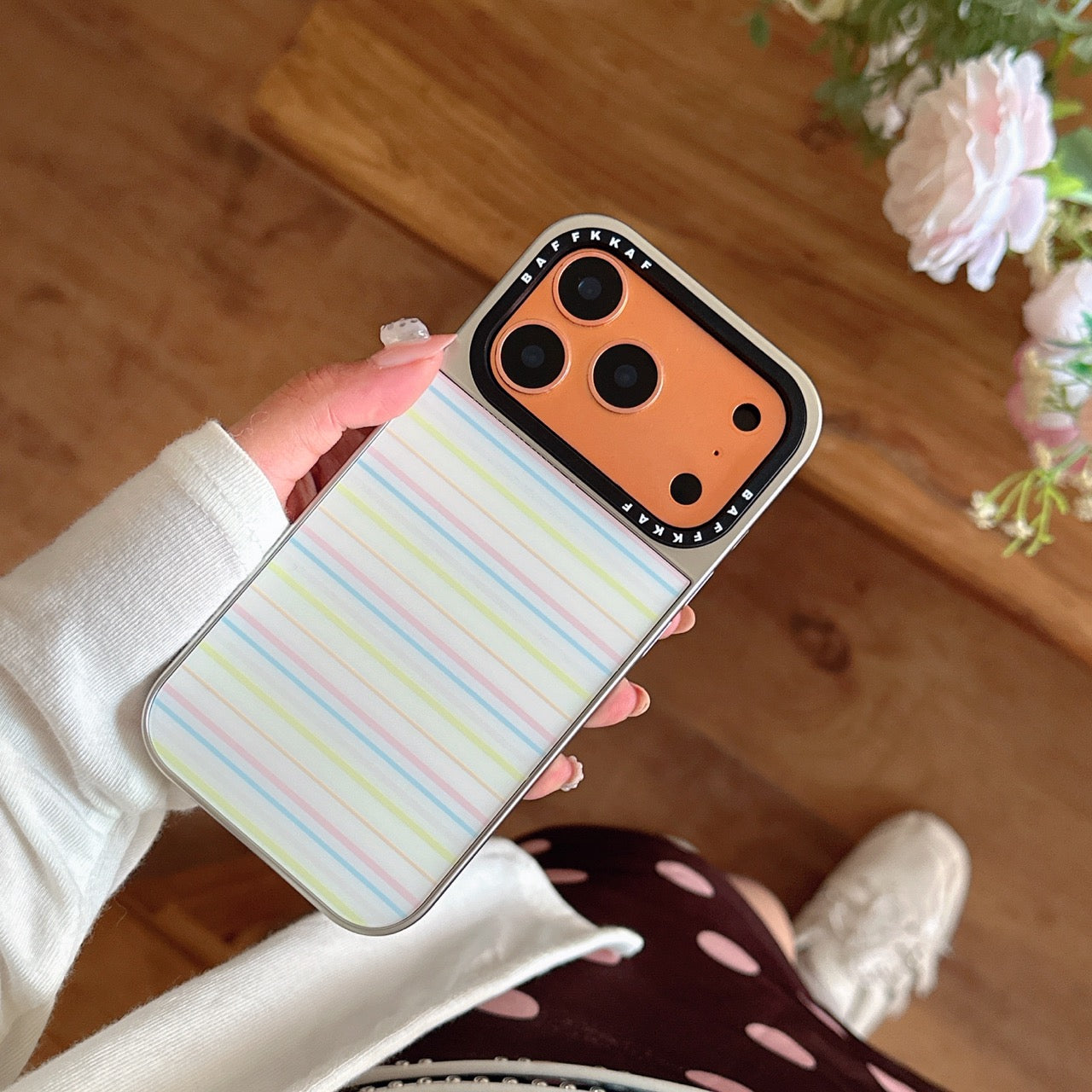 Top-down view of a hand holding the orange gold camera variant of the striped phone case with flowers.