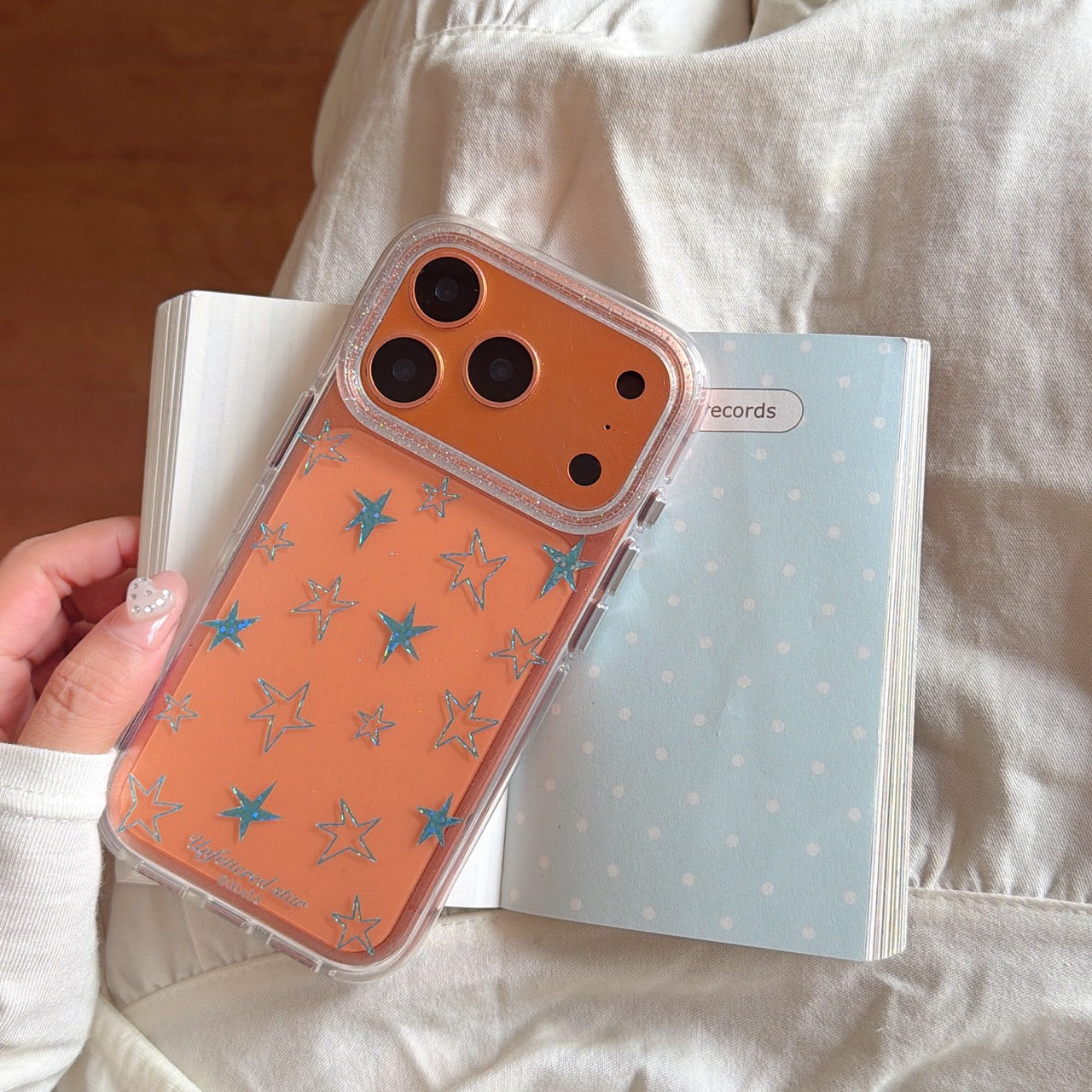An orange holographic star phone case placed on top of an open pastel notebook.