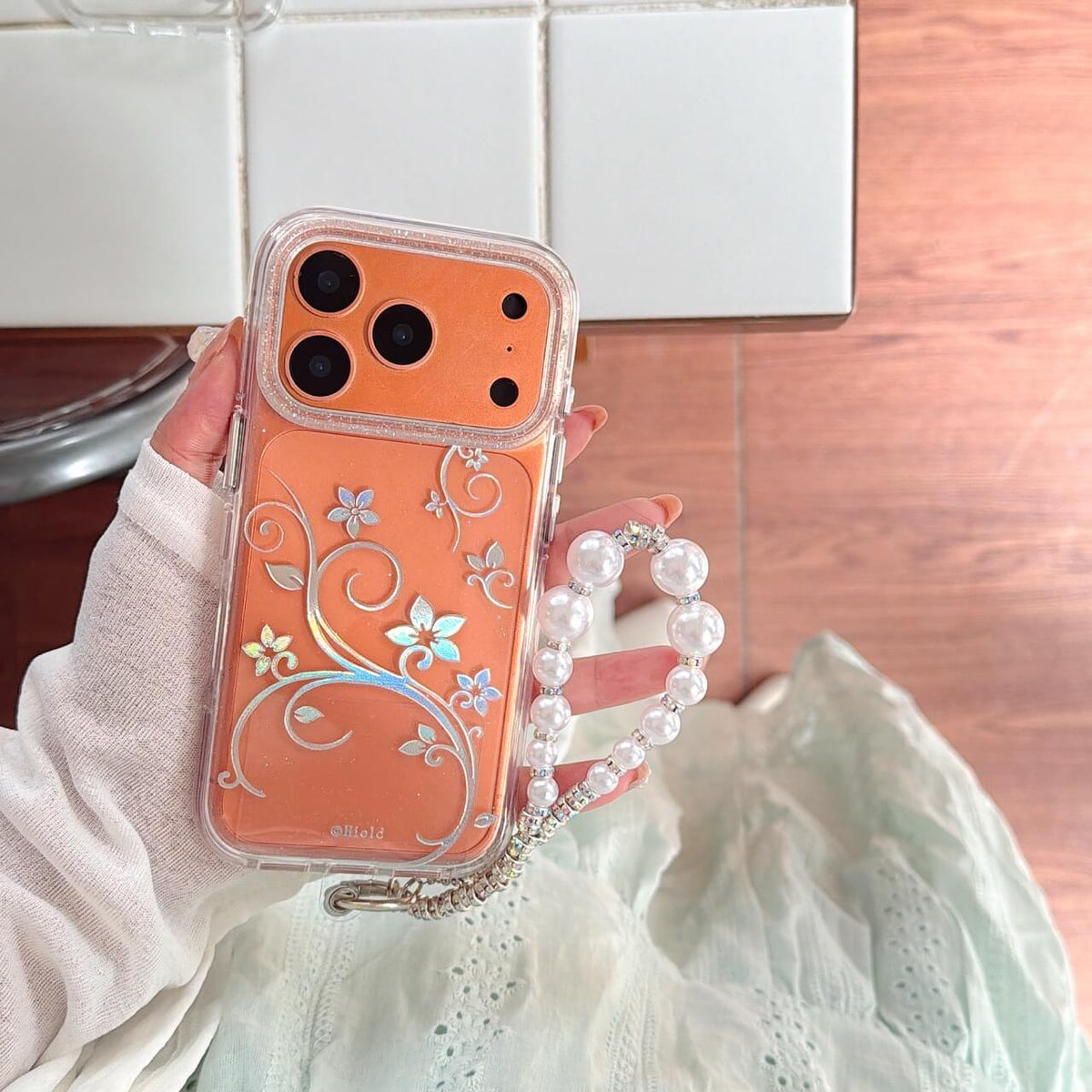 Orange iPhone with iridescent floral clear case and pearl wrist strap