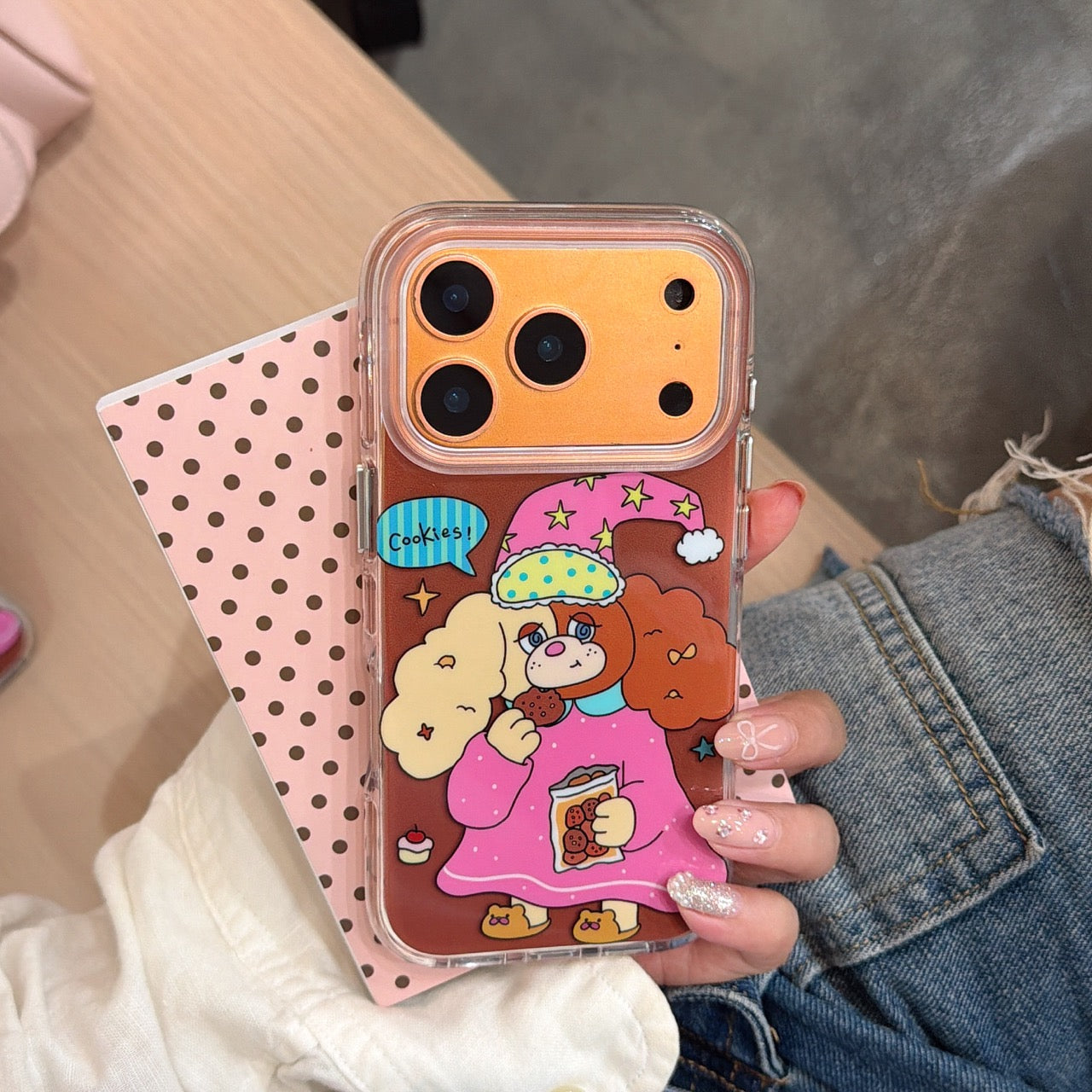 A close-up of a hand holding the orange metallic camera frame cartoon dog case against a pink polka dot card.