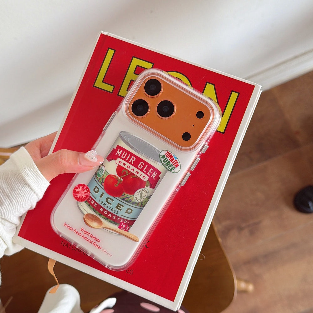 A hand holding the orange metallic camera frame tomato case over a bright red vintage book.
