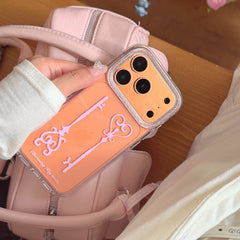 A hand holding an orange metallic charming key phone cover against a pastel pink quilted leather handbag.