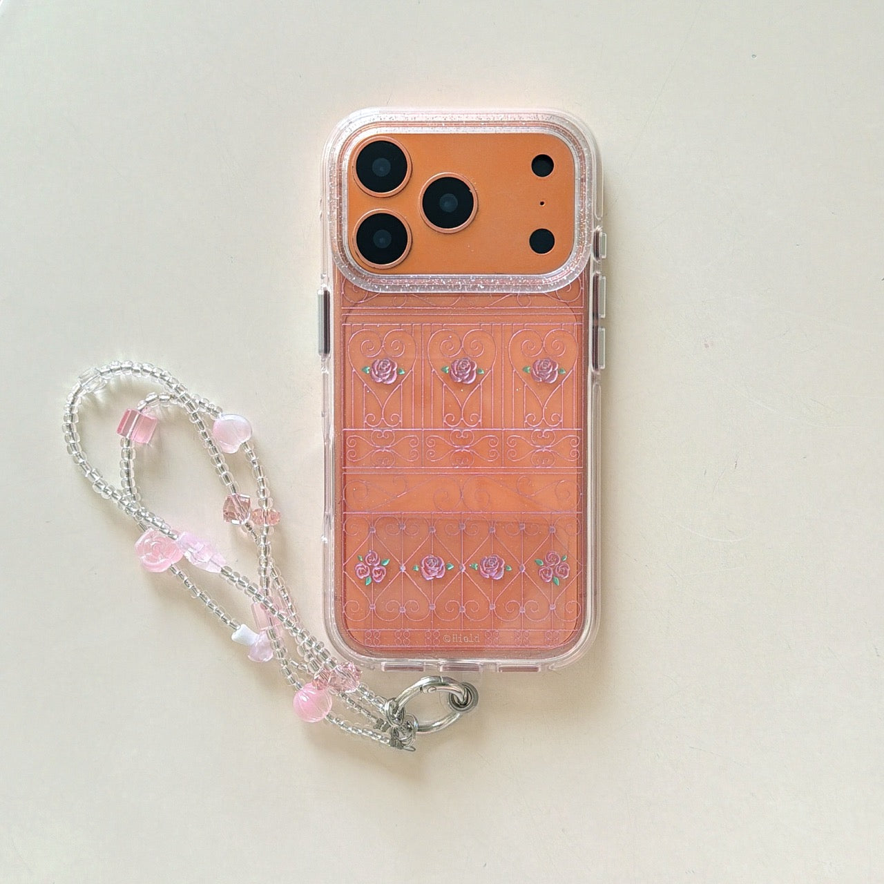 Product shot of an orange rose gate clear phone case with a matching pink beaded strap.