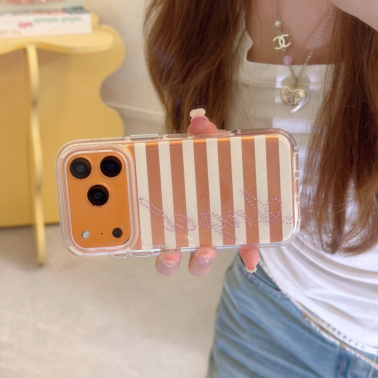 Close-up of a horizontal orange and white striped iPhone case with sparkling rhinestone Angel lettering and a metallic orange camera frame.