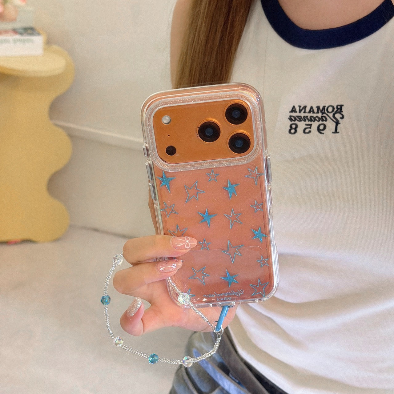A hand holding an orange clear phone case featuring blue stars and a beaded lanyard.