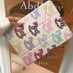 A hand holding an origami folding magnetic smart ipad cover diagonally in front of a glass door, highlighting the vibrant and playful pattern.
