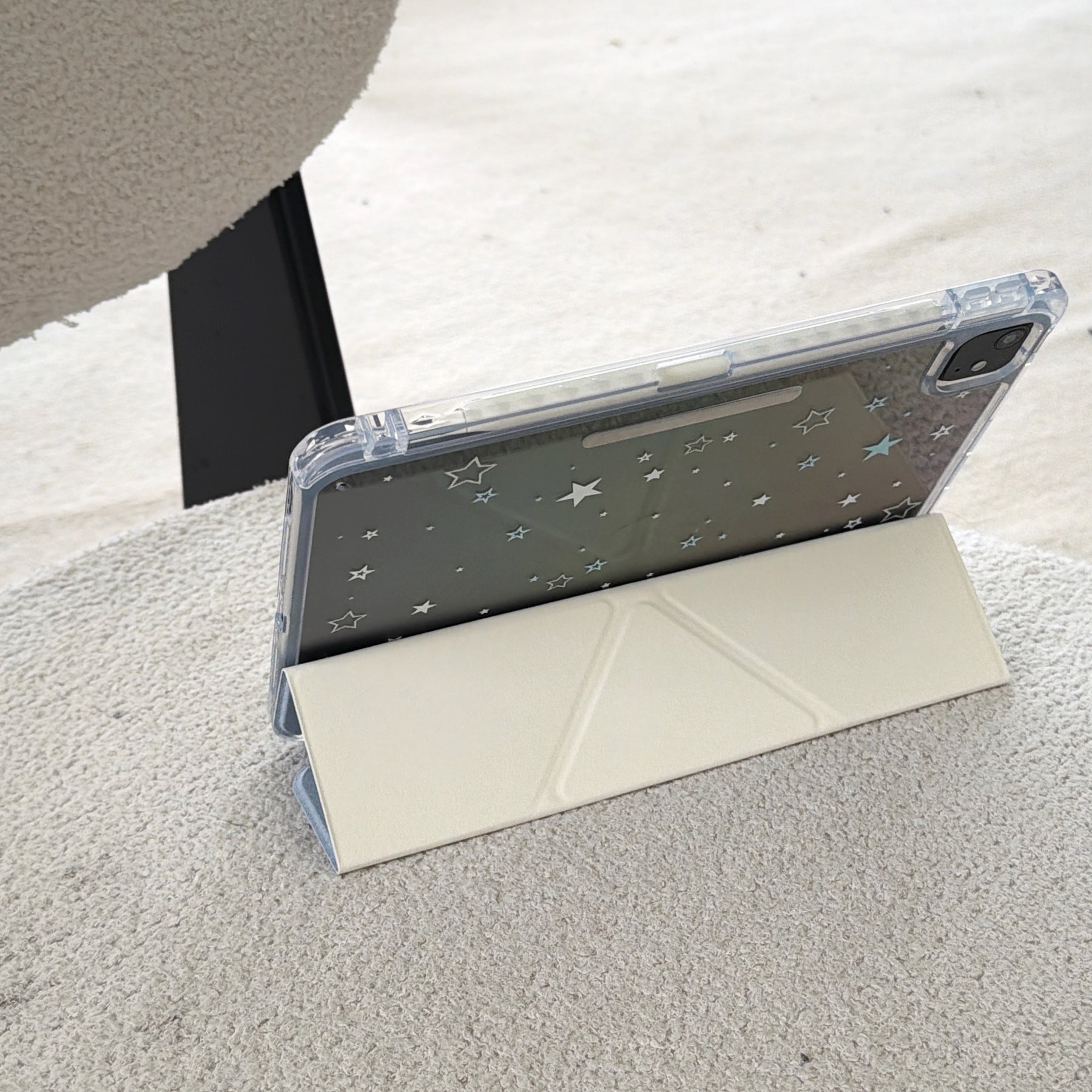 An iPad propped up horizontally on a white textured surface using a cream geometric origami folding stand cover.