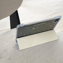 An iPad propped up horizontally on a white textured surface using a cream geometric origami folding stand cover.