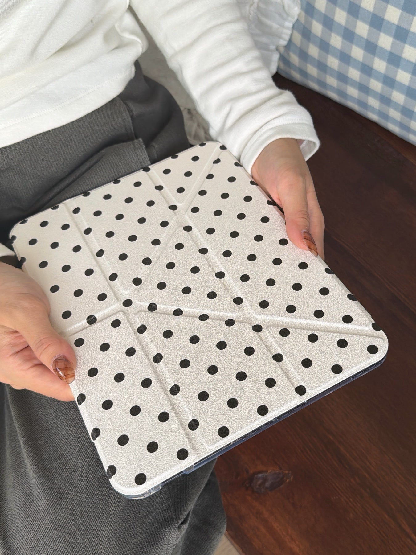 A person wearing a white long-sleeve shirt holding a closed ivory white origami folding stand ipad cover featuring small black polka dots.