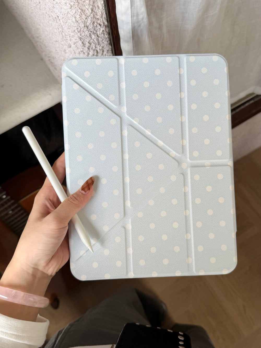 A handheld view of a closed light blue origami stand iPad cover with white polka dots and a white stylus pen.