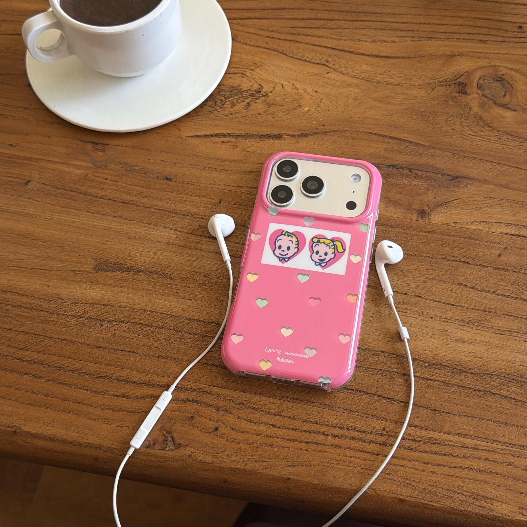 An Osamu Goods pink case on a wooden coffee table next to a white ceramic cup and white earphones.