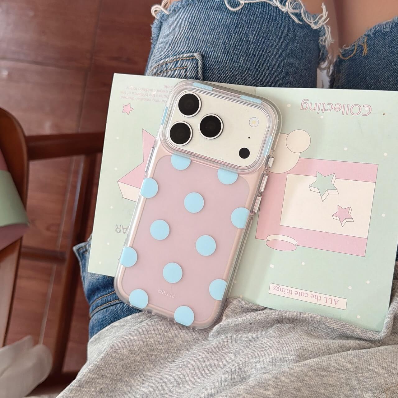 Pastel pink iPhone case with blue raised dots in a lifestyle setting