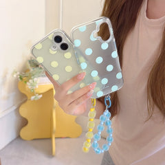 A girl holding green and clear polka dot iPhone cases with matching yellow and blue jelly beaded wrist straps.