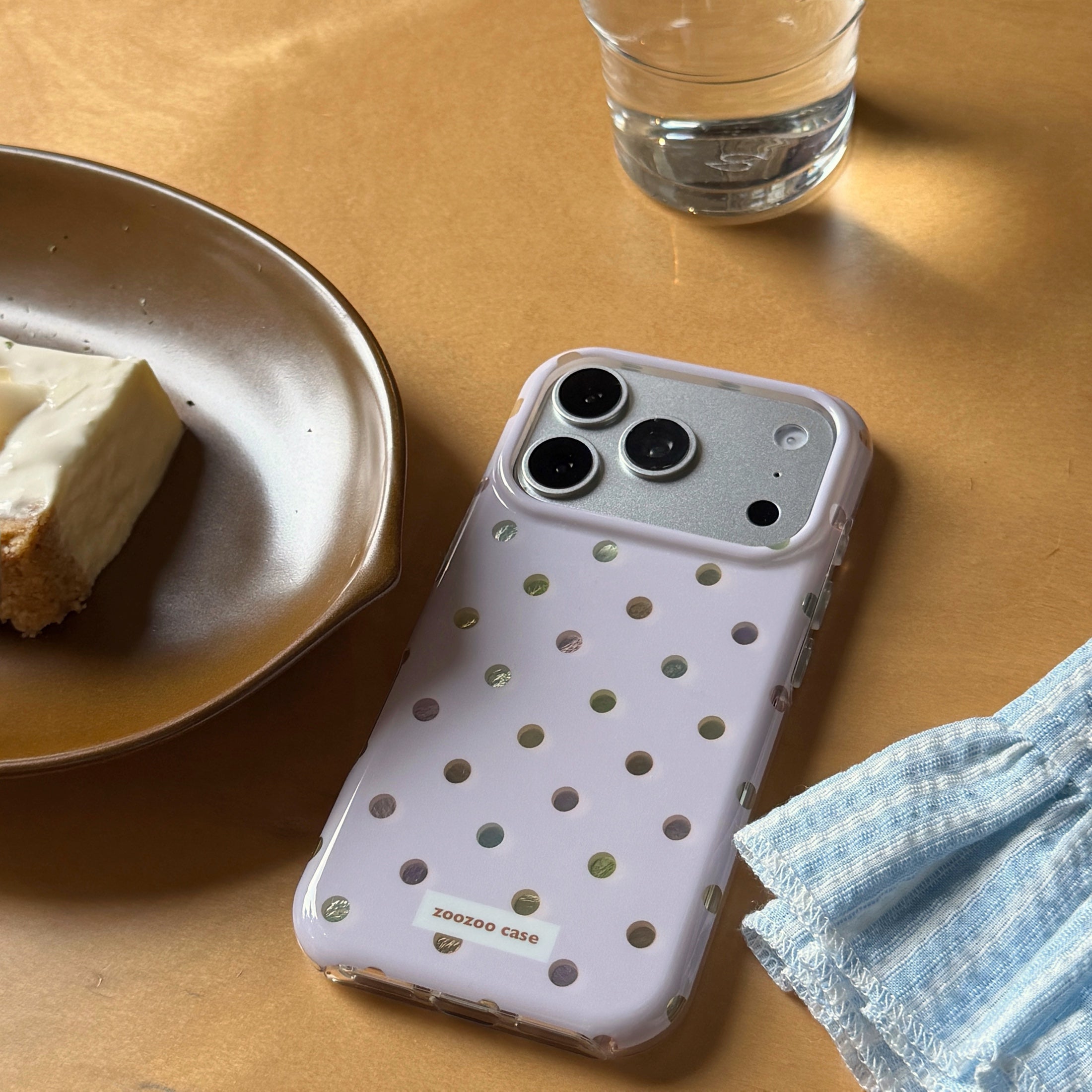 A pastel purple holographic polka dot iPhone case on a wooden table next to a plate of cake.