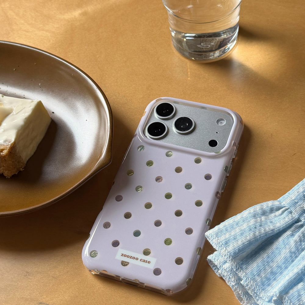 A pastel purple holographic polka dot iPhone case on a wooden table next to a plate of cake.
