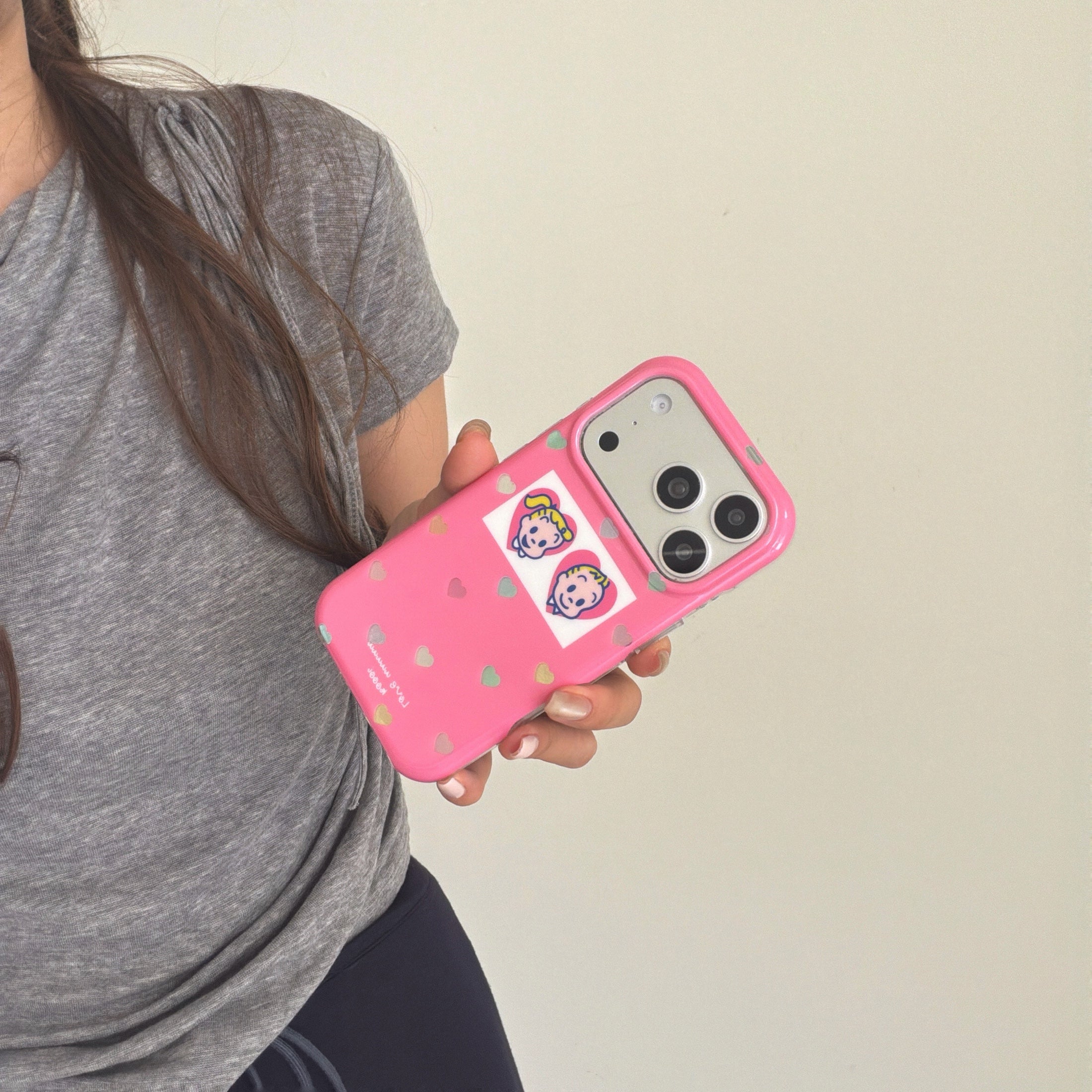 A hand holding a pink glitter heart phone case at a dynamic angle against a plain background.