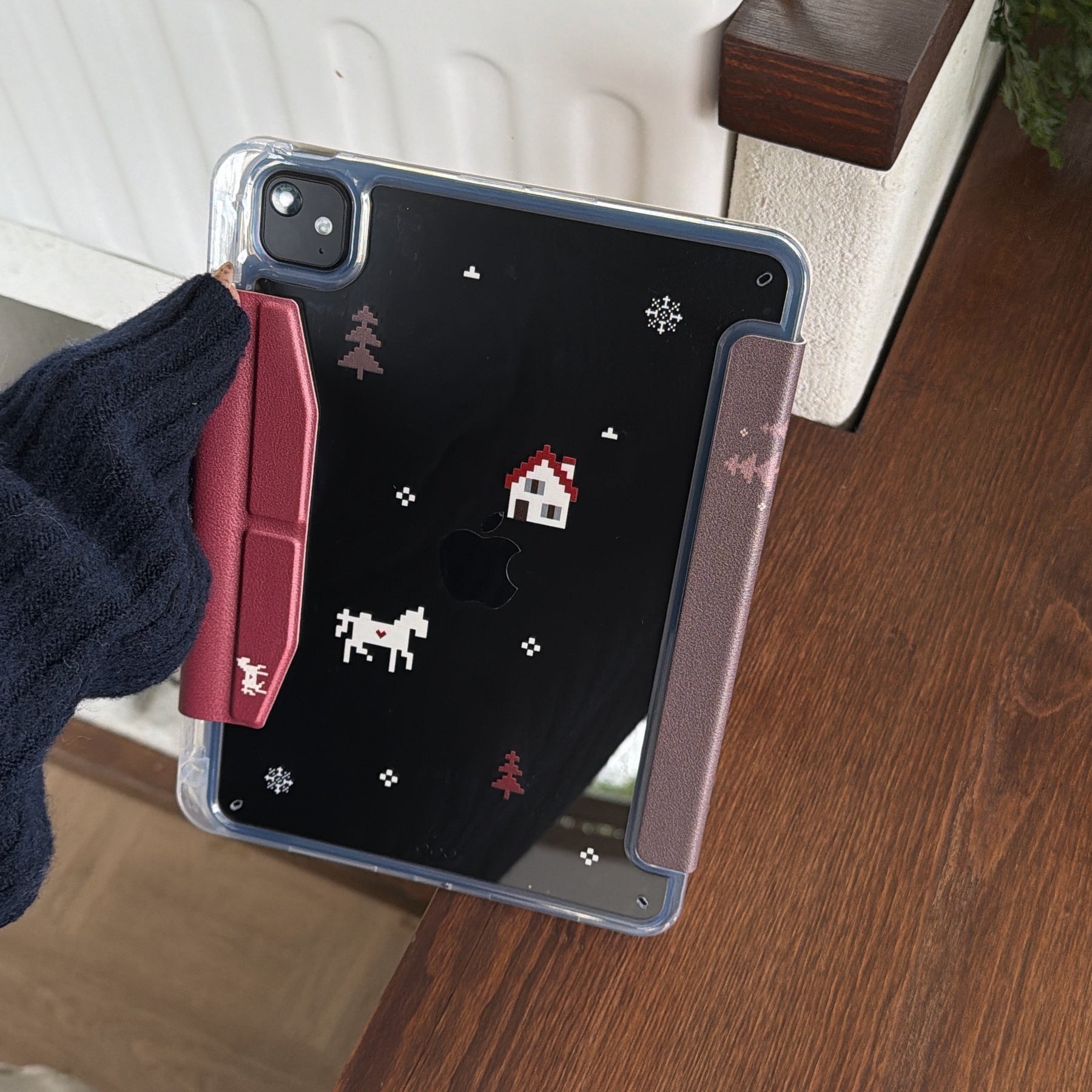 The back view of an iPad in a shockproof clear back case decorated with cute pixel art graphics of a house, reindeer, and snowflakes with a red magnetic flap.