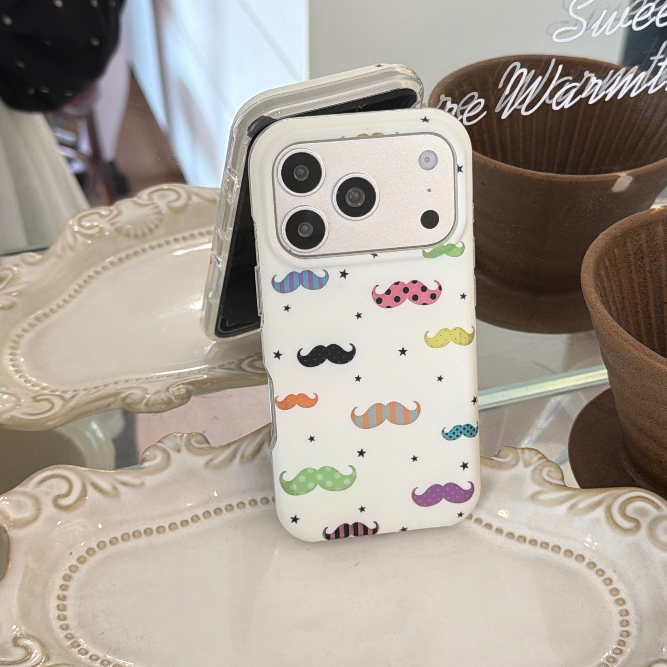 A quirky white mustache phone case standing vertically on an elegant white ceramic display tray.