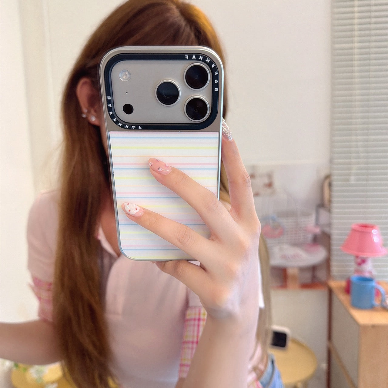 A close-up mirror selfie showing a rainbow striped aesthetic phone cover on an iPhone.