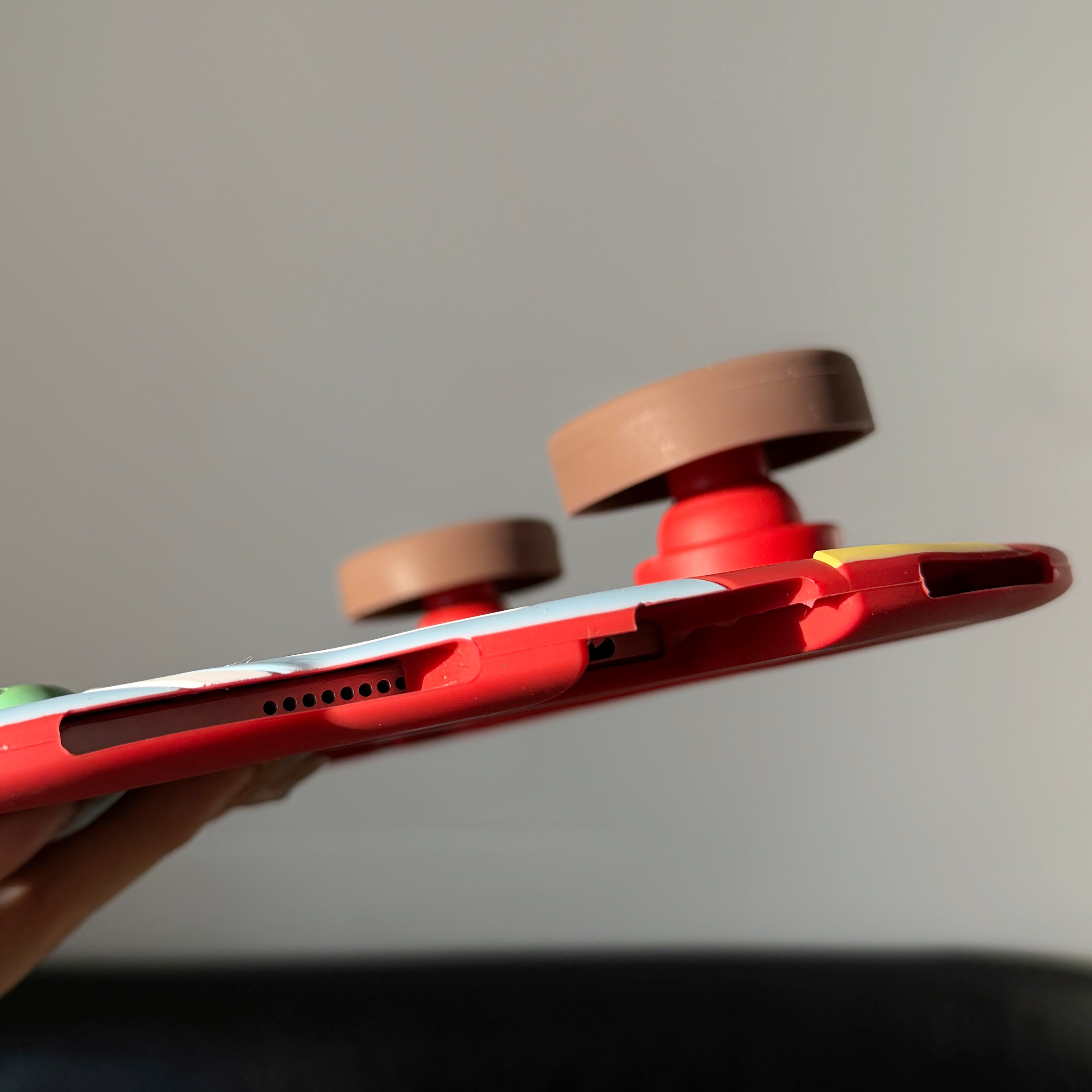 Close-up side view of a red silicone bus iPad case, showing the precise speaker and charging port cutouts on the bottom edge and the side profile of two thick brown wheel kickstands.