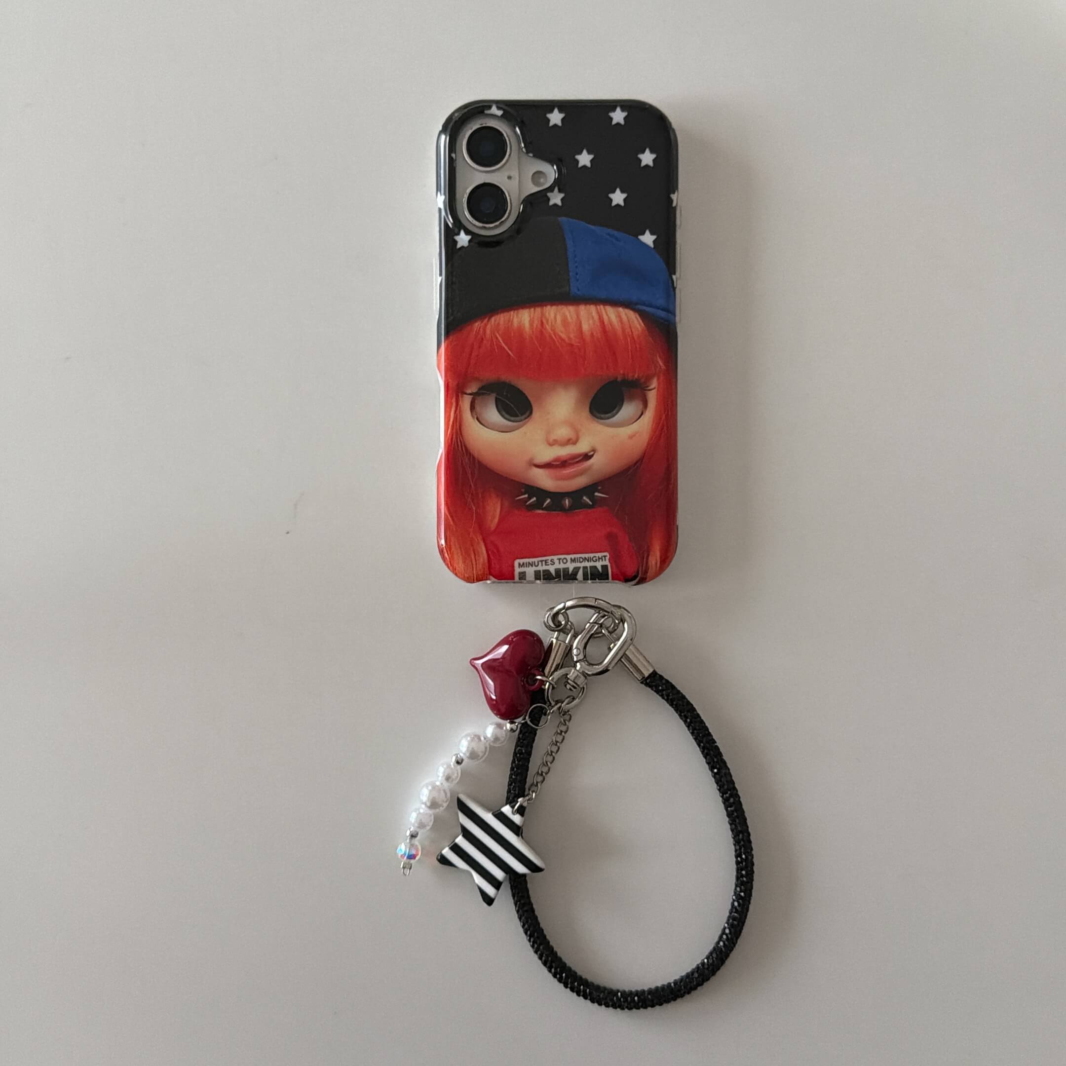 Red-haired doll iPhone case with black wrist strap and striped star charm.