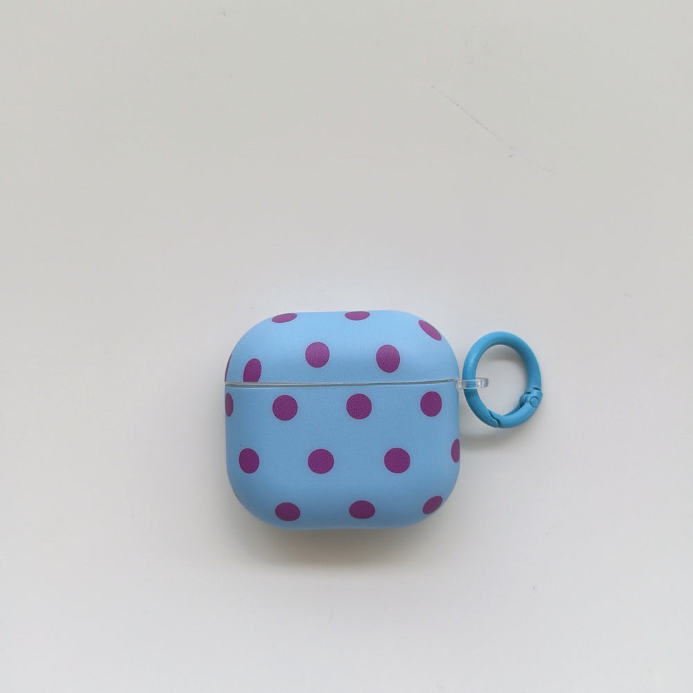 Front view of a light blue AirPods case with purple polka dots and a matching circular clip ring on a plain white background.