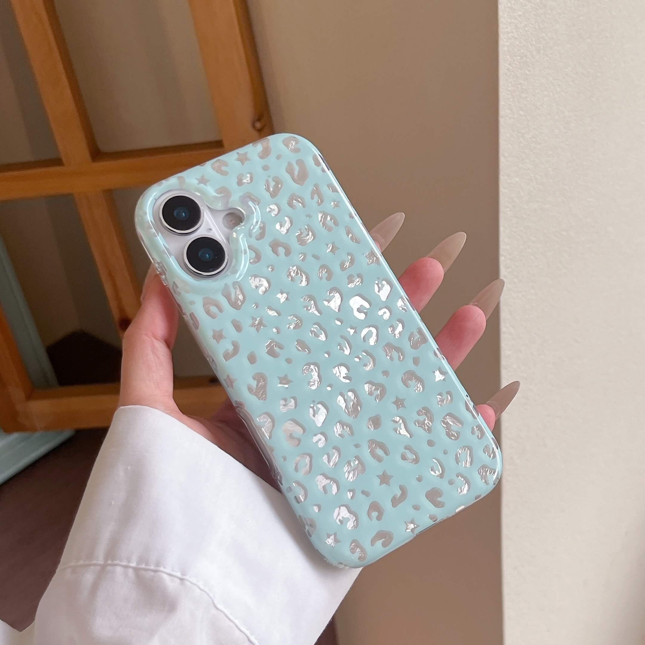 A hand showcasing a shiny mint green foil star leopard iPhone case with a fluid wavy design.