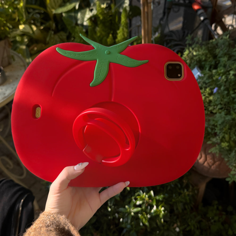 A hand holding a shockproof kids ipad case with stand upright against a blurry green garden background, emphasizing its bold red color and large protective shape.