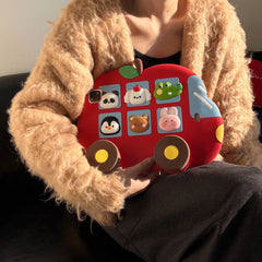 A lifestyle shot of a person in a plush brown sweater sitting on a black leather sofa, holding the shockproof silicone kids iPad case horizontally to show the playful 3D design.