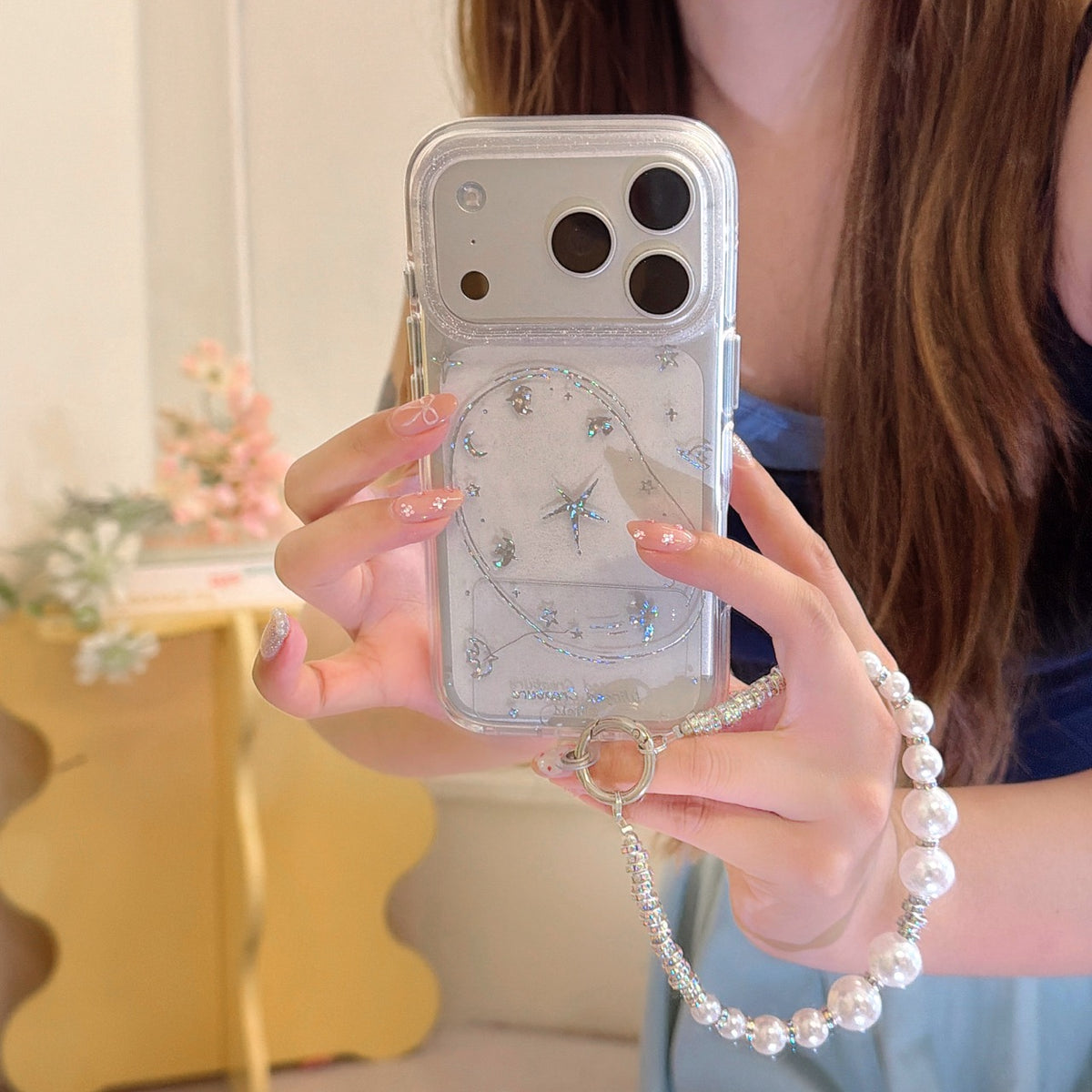 Close-up of a silver glitter galaxy iPhone case featuring a North Star design, metallic lens armor, and a chunky white pearl bead bracelet strap.