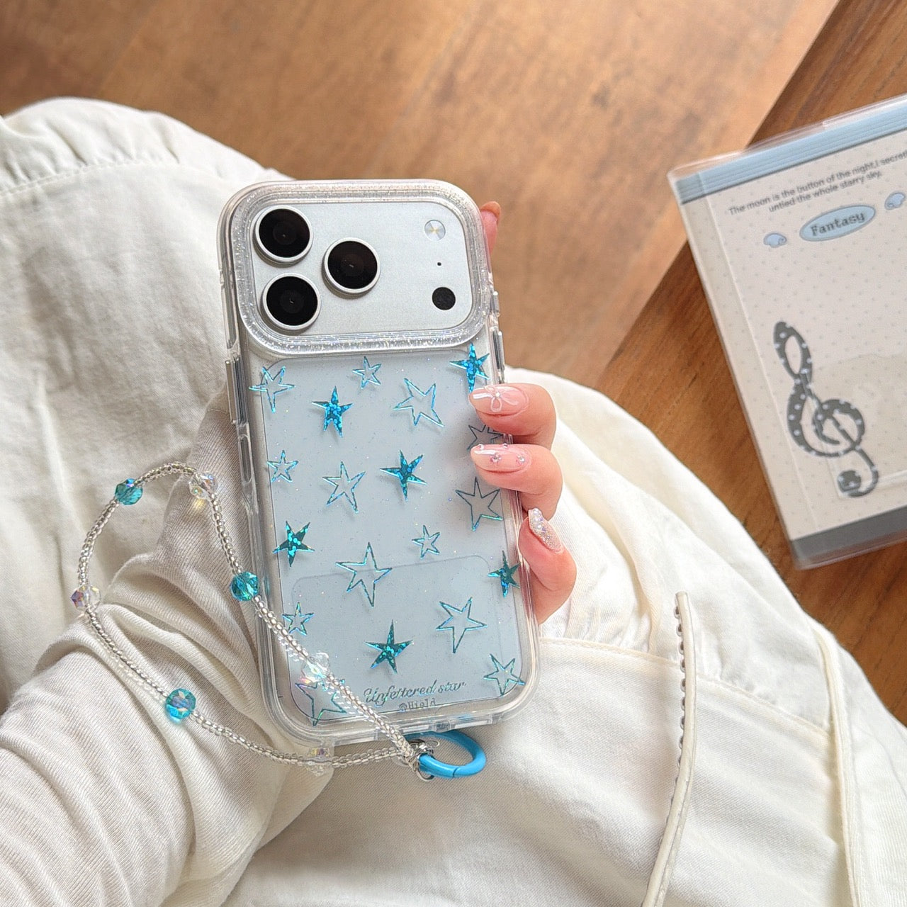 A silver glitter star iPhone case with a crystal beaded strap resting on a white dress.