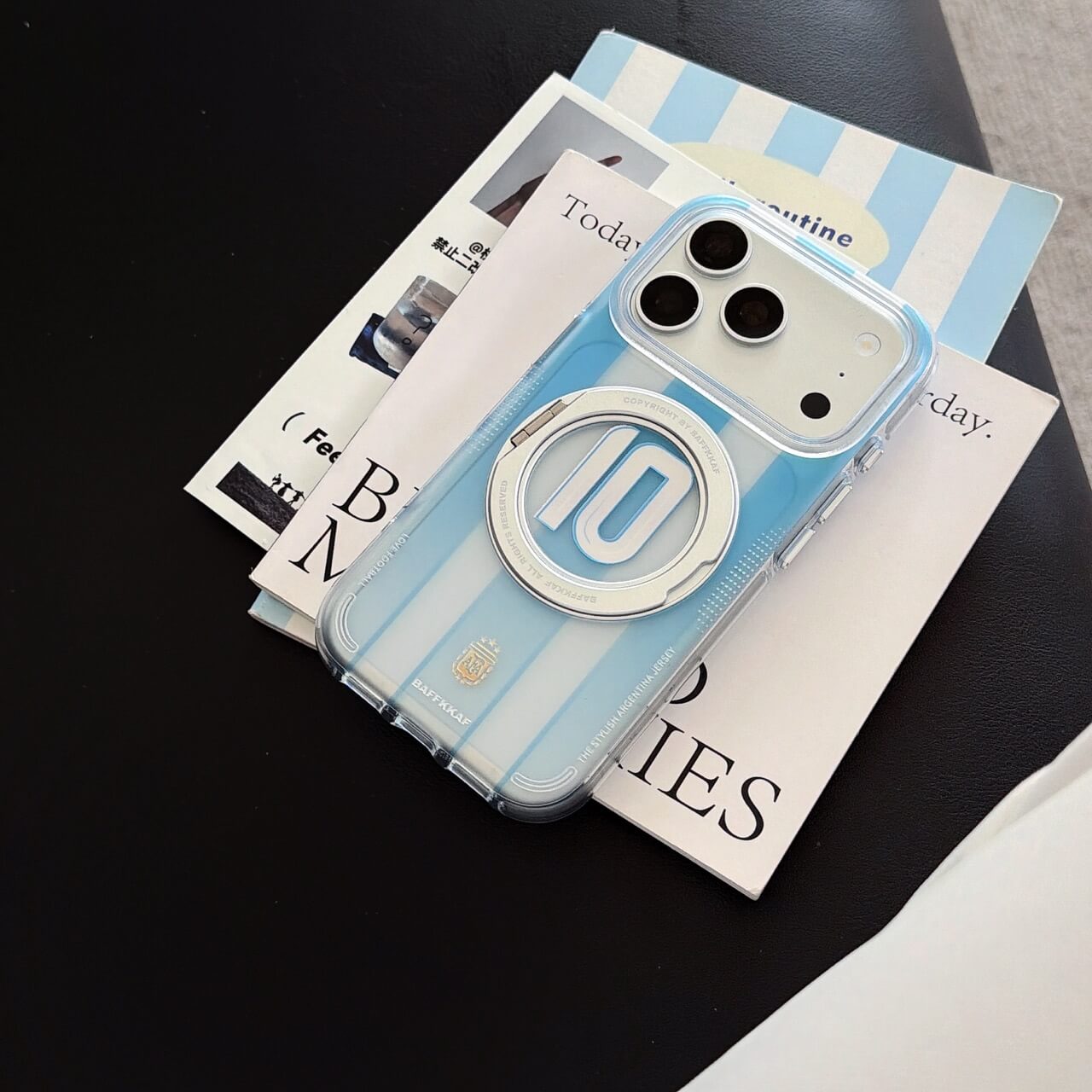 An Argentina sky blue soccer stripe iPhone case lying flat on magazines.