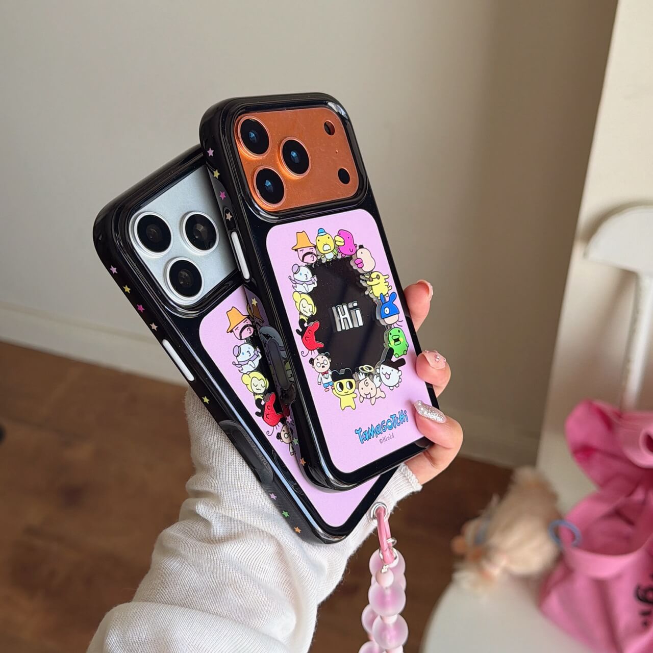 Hand holding stacked Tamagotchi phone cases showcasing the star-patterned black shockproof bumper edges.