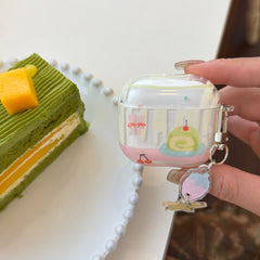 A hand holding a sweet dessert AirPods case next to a green matcha layered pastry on a table.