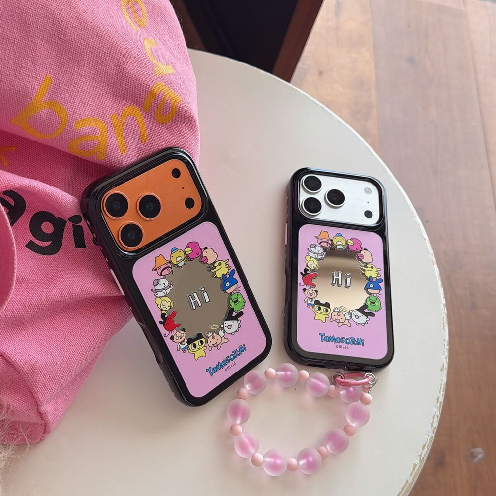 Two Tamagotchi mirror iPhone cases in silver and orange colors on a white tabletop with a pink beaded strap.