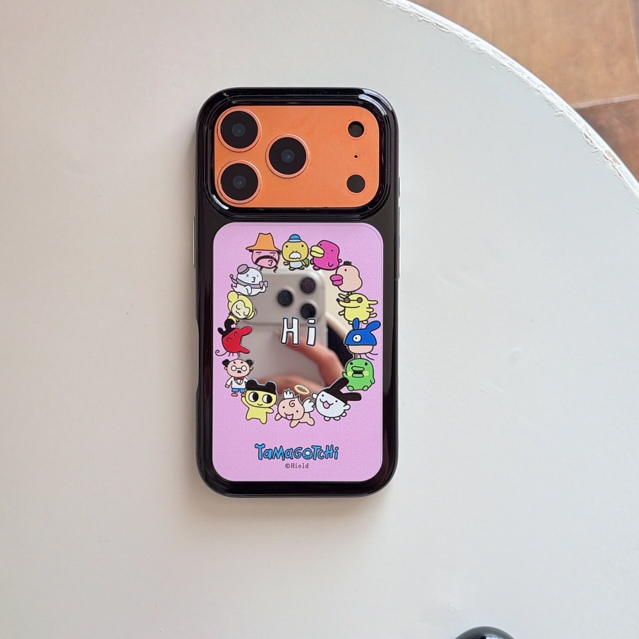 Flat lay of the Tamagotchi mirror phone case with an orange camera plate on a white background.