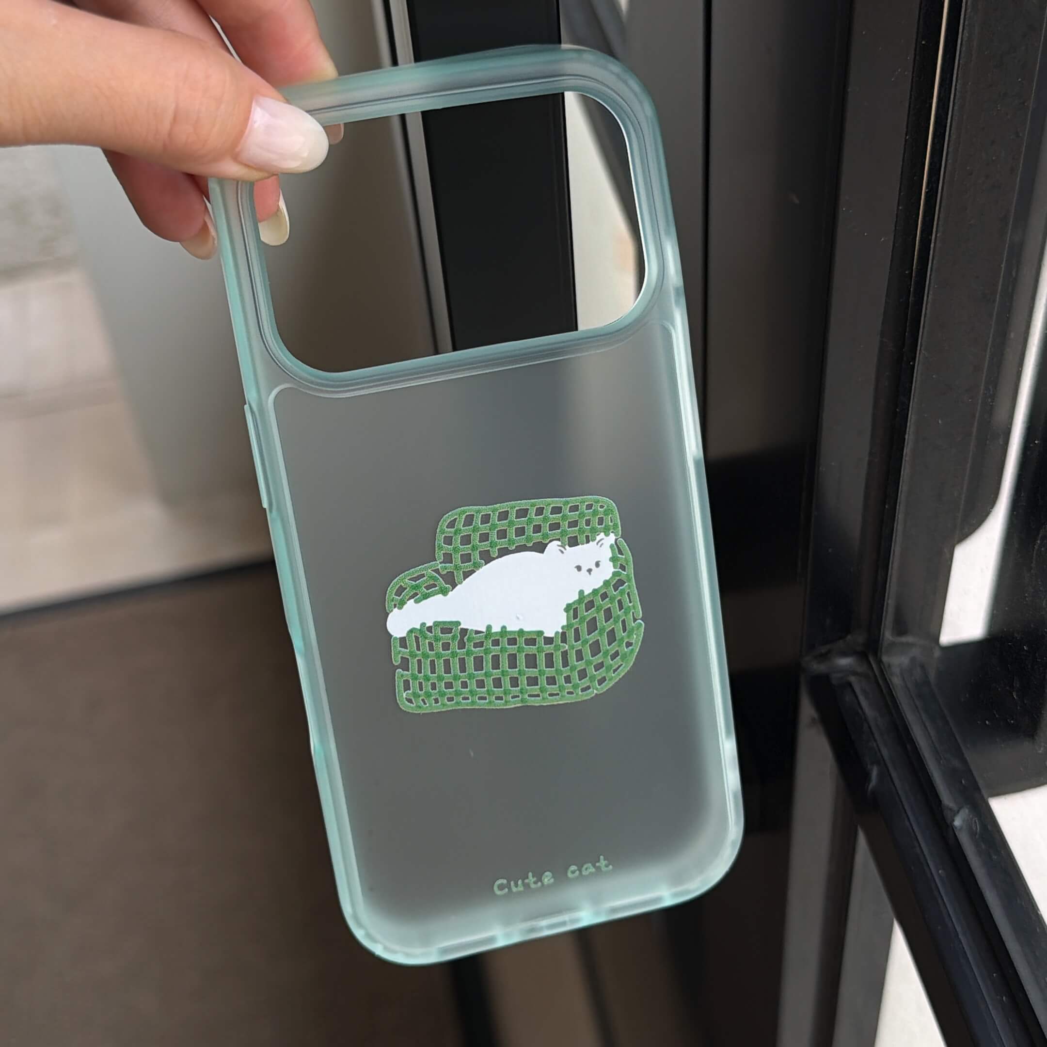 A hand holding a transparent mint green iPhone case showing the couch cat graphic insert.