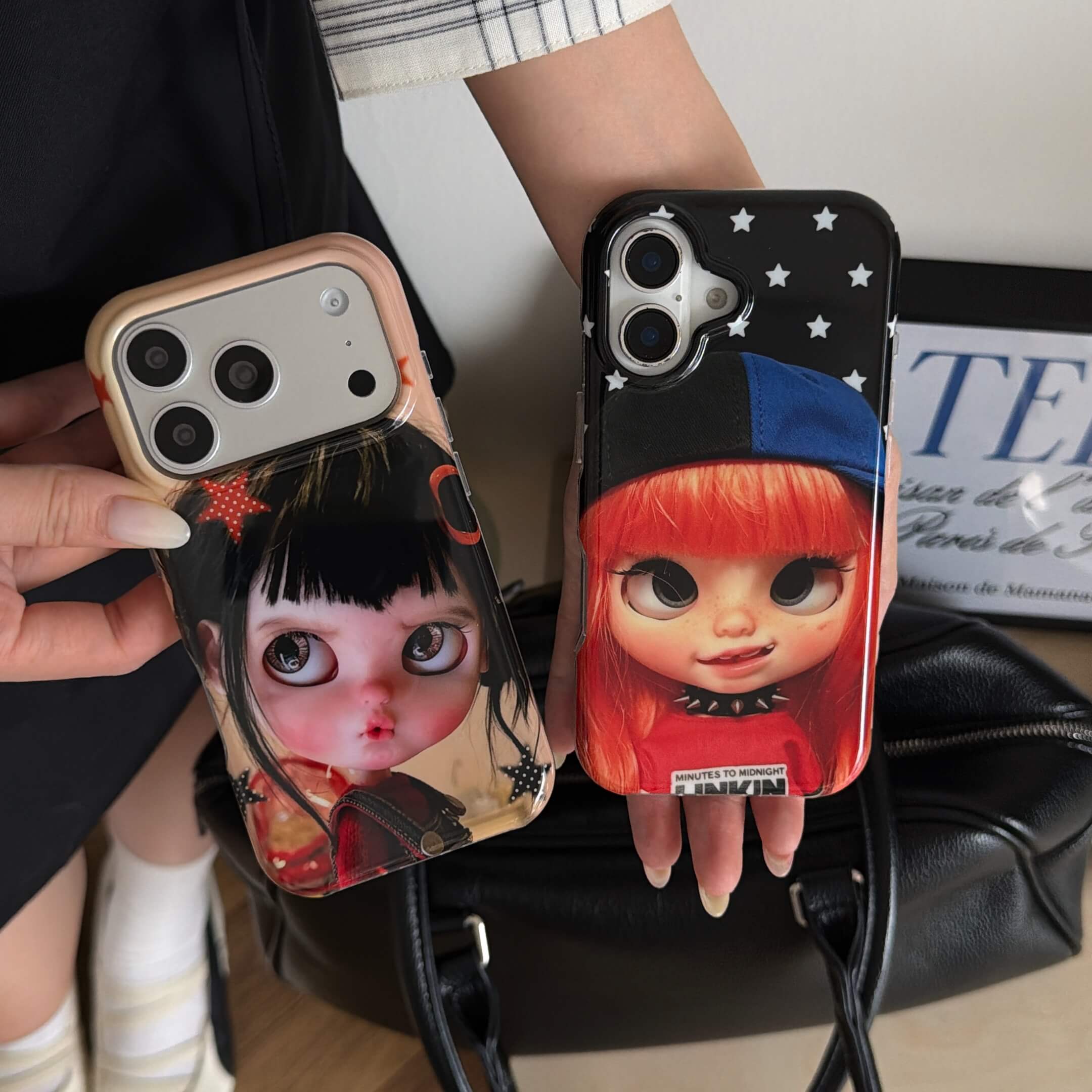 Two big-eye doll iPhone case styles displayed above a black handbag.