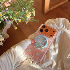 An orange iPhone in a luxury floral shell-texture case with a flower grip stand, resting on a girl's lap.