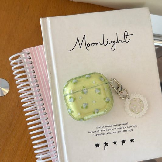 A vintage floral green AirPods case resting on a white Moonlight journal next to a pink spiral notebook.