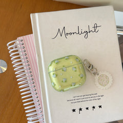 A vintage floral green AirPods case resting on a white Moonlight journal next to a pink spiral notebook.