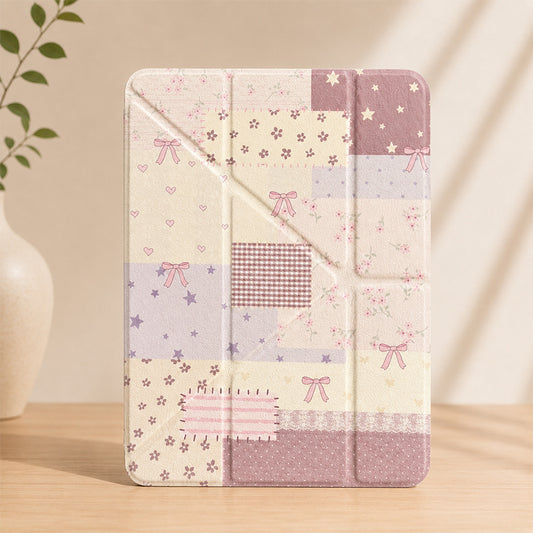 A cottagecore vintage patchwork iPad case standing vertically on a light wood table with a white ceramic vase in a soft shadow background.