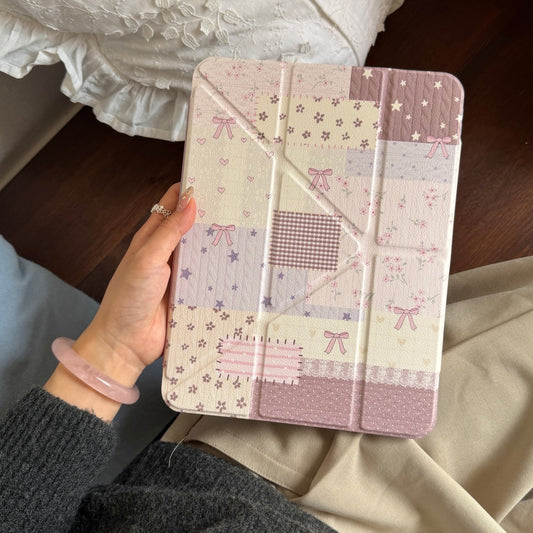 A person wearing a pink jade bangle holding a vintage ribbon bow patchwork iPad folio case vertically against a white ruffled pillow.