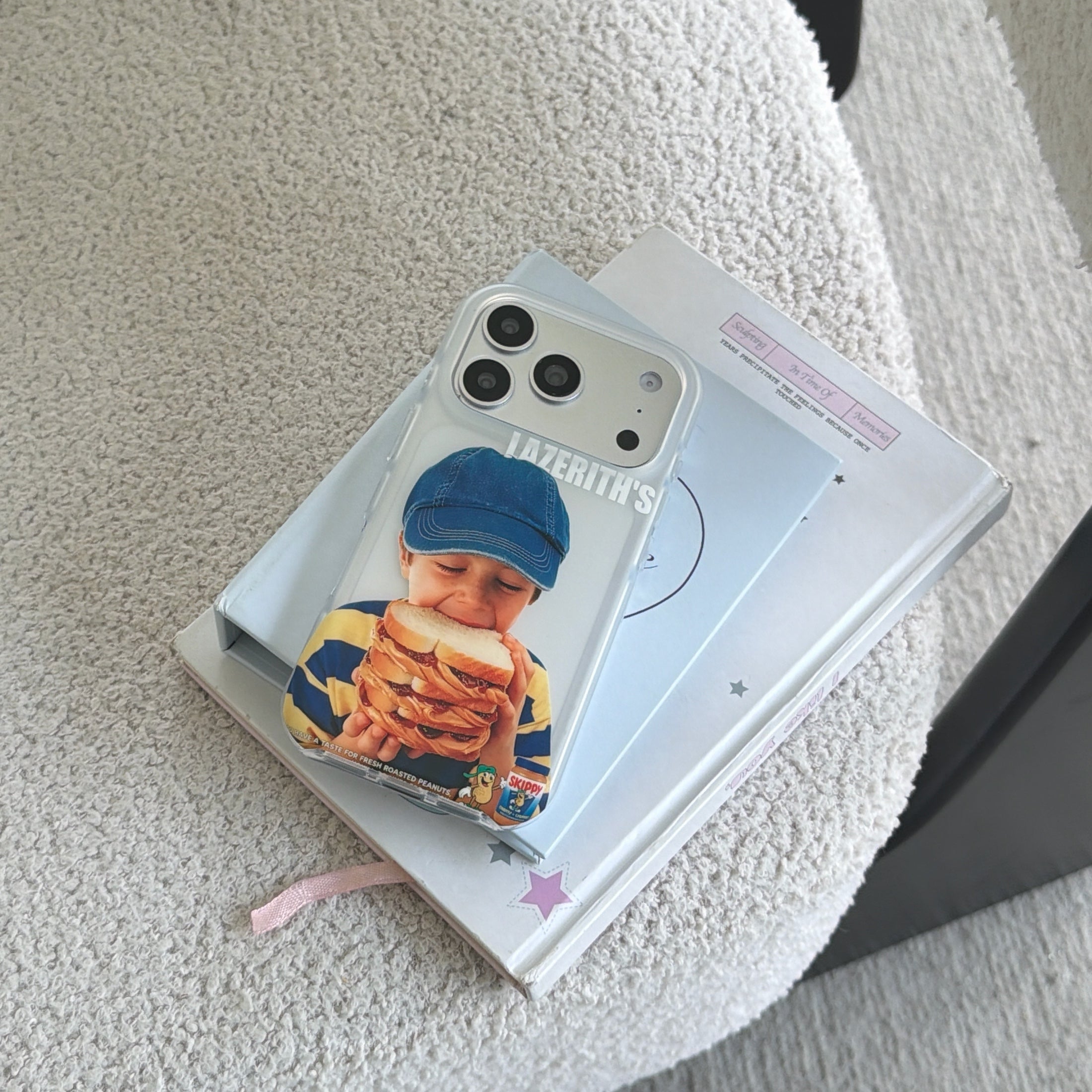 A vintage sandwich boy phone case resting on a stack of books on a white bouclé chair.