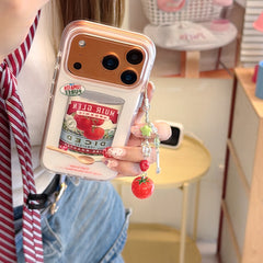 A close-up of a hand holding a vintage tomato soup phone cover featuring an orange metallic lens protection frame.