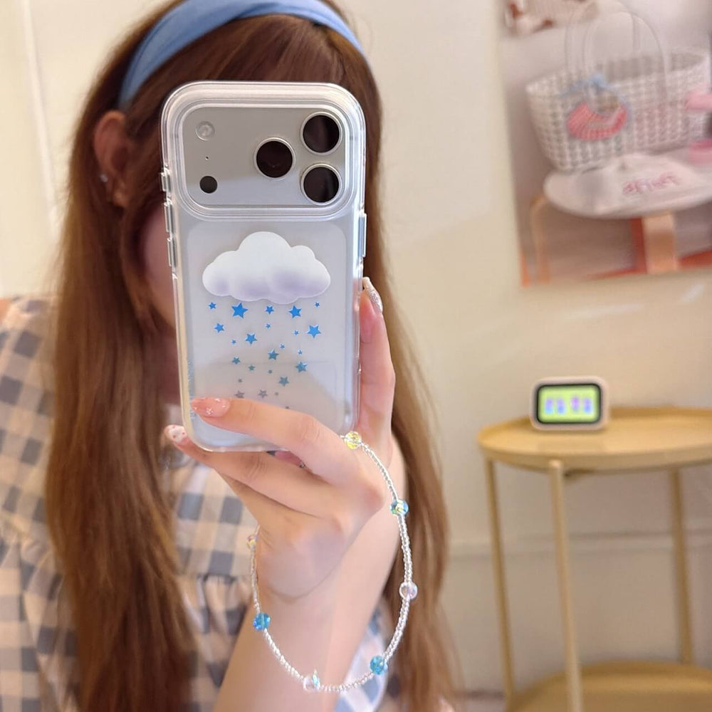 A clear iPhone case with a 3D white cloud and blue twinkle stars resting on an open pastel notebook.